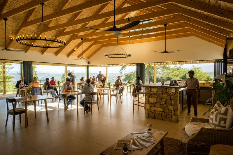 Modern interior of a lodge with wooden beams and large windows, people sitting at tables.